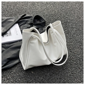 Vue à plat d'un cabas en similicuir blanc avec magazine et veste noire sur asphalte