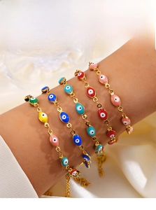 Gros plan de bracelets œil de nazar colorés en émail doré superposés sur fond satiné