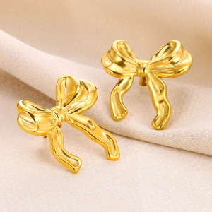 Detailed view of golden ribbon bow earrings on a beige textured fabric background