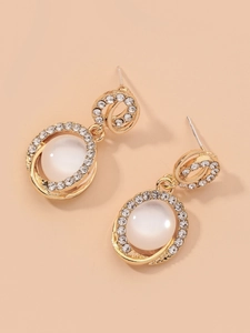 Détail de boucles d'oreilles dorées avec pierres œil de chat et strass étincelants
