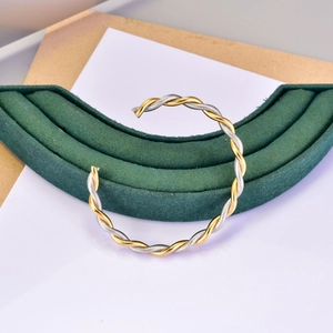 Detail of twisted cable bangle featuring a contrast of gold finish and silver textures