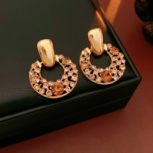 Détail de boucles d'oreilles vintage dorées serties de strass champagne sur cuir noir