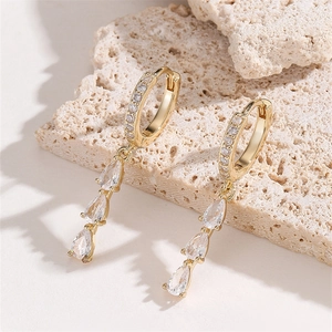 Sparkling gold teardrop hoop earrings with white zircon on a natural stone background