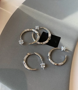Detail of silver twisted C-shaped hoop earrings with micro-pave zircons and silicone backs