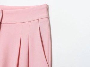 Detailed macro view of pink trousers' waistline featuring pleats and pocket stitching