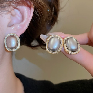 Close-up of vintage oval stud earrings with grey cat-eye stone and gold zircon pavé frame
