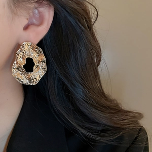 Close-up of oversized gold geometric earrings with a hammered texture and cutout design
