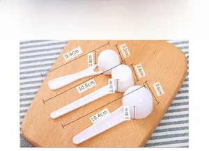 Three assorted white plastic measuring spoons on a wooden board for kitchen powder dosing