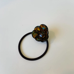 Detailed view of amber resin flower hair tie with black elastic cord on white surface