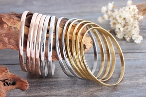 Detailed shot of gold, silver, and rose gold polished titanium steel bracelets on wood