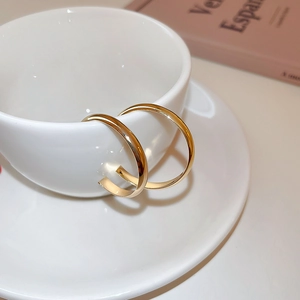 Close-up of minimalist golden C-shaped metal earrings resting on a white ceramic cup