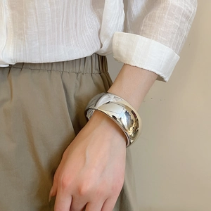 Detailed view of wide silver-tone cuff bracelet with polished mirror surface on wrist