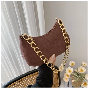 Dettaglio borsa a mezzaluna in camoscio marrone con catena dorata su sfondo vintage
