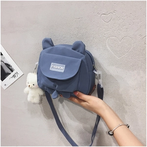 Detail of blue nylon bear-shaped crossbody bag featuring a plush white bear charm accessory