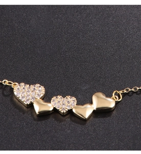 Macro shot of gold heart necklace with zircon inlay and polished hearts on black background