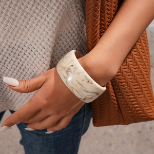 Detail of cream marbled resin bangle worn by model with textured fashion accessories