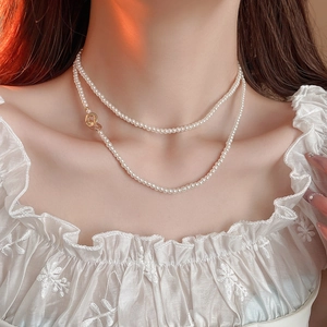 Double-layer minimalist pearl necklace with a circular gold clasp on a female model