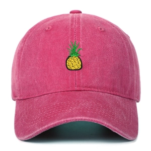 Close-up of yellow pineapple embroidery on a distressed rose red washed cotton baseball cap