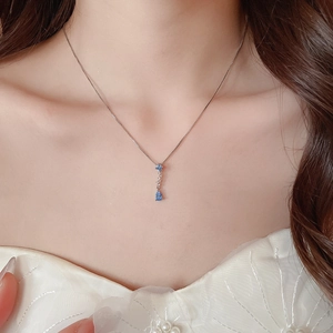Close-up of elegant silver chain with blue zircon star and pear-shaped pendants on collarbone