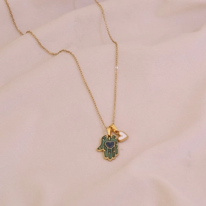 Gold Hamsa Hand necklace with green enamel pendant and white heart on soft pink fabric