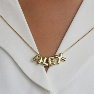 Polished gold bubble letter necklace with ALEX pendant shown on a white V-neck dress
