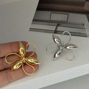 Detailed view of large gold and silver metallic floral earrings held in hand for scale
