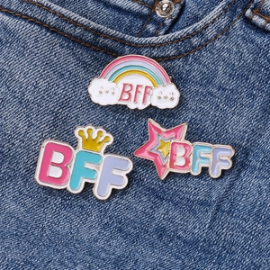 Three-piece BFF rainbow cloud and star enamel pins set on blue denim fabric background