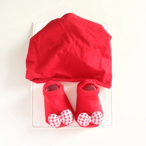 Red cotton knit baby hat and matching socks set with white checkered bows on white backdrop