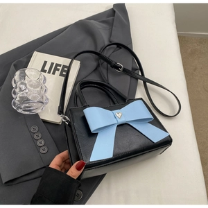 Detail of black crossbody bag with large blue bow and heart zircon on white bed
