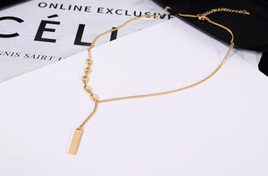 Macro detail of 18K gold plated bar pendant and coffee bean chain links on gold necklace