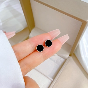Macro view of minimalist black shell stud earrings held to show relative size