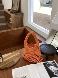 Detail of an orange macrame cotton rope woven tote bag on a sunlit wooden windowsill