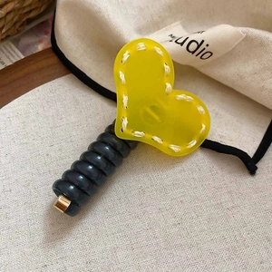 Détail d'un élastique à cheveux cœur en acrylique jaune avec coutures blanches
