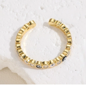 Dettaglio macro di anello placcato oro con motivo occhio del male in smalto e zirconi