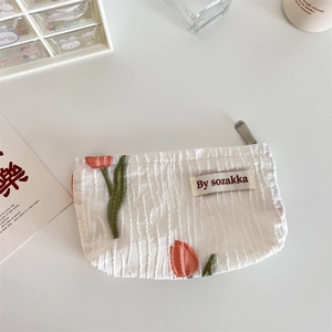 Detail of floral embroidery and pleated texture on a white fabric cosmetic clutch bag