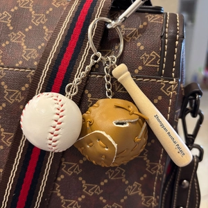 Macro detail of mini baseball keychain with wood bat and leather glove on a luxury bag