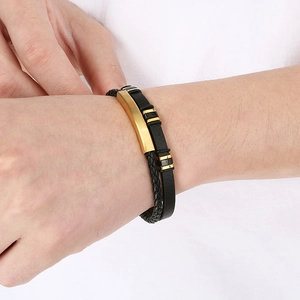 Detail of double-layer black braided leather bracelet with golden curved metal plate