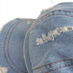 Close-up of distressed light blue denim octagonal hat with ripped details and orange stitching
