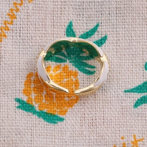 Top view of a gold-plated adjustable wavy ring with white enamel finish on a textured fabric