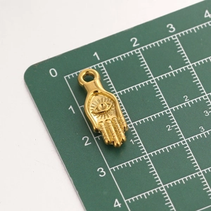 Detailed macro view of 18k gold plated stainless steel Hamsa hand pendant on scale board