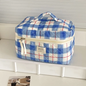 Blue and red plaid quilted makeup bag with handle and zipper in a minimalist home setting