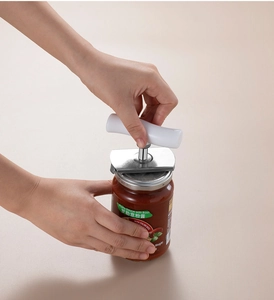 Manual stainless steel can opener with white handle opening a jar of pasta sauce