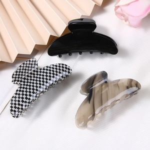 Three acetate hair claws in black, checkered, and marble patterns on a decorative desk