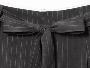 Detail of grey pinstripe high-waist trousers featuring a decorative tie-up bow belt