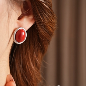 Close-up of a silver-tone oval earring with a smooth red enamel stone on a model's ear