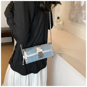 Blue denim texture cylinder bag with silver trim and metal chain strap on model