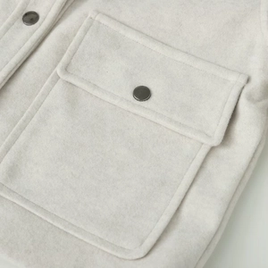 Detail view of cream shacket fabric featuring flap pocket and dark metallic button