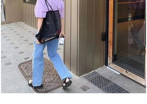 Street style shot of a spacious black mesh tote bag paired with light wash ripped jeans