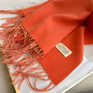 Close-up of orange cashmere-like scarf texture with fringe detail and woven brand label