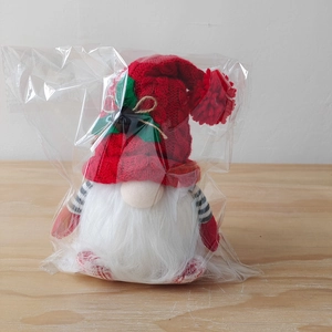 Detail of a Christmas gnome plush with red knitted hat and stripes in clear packaging